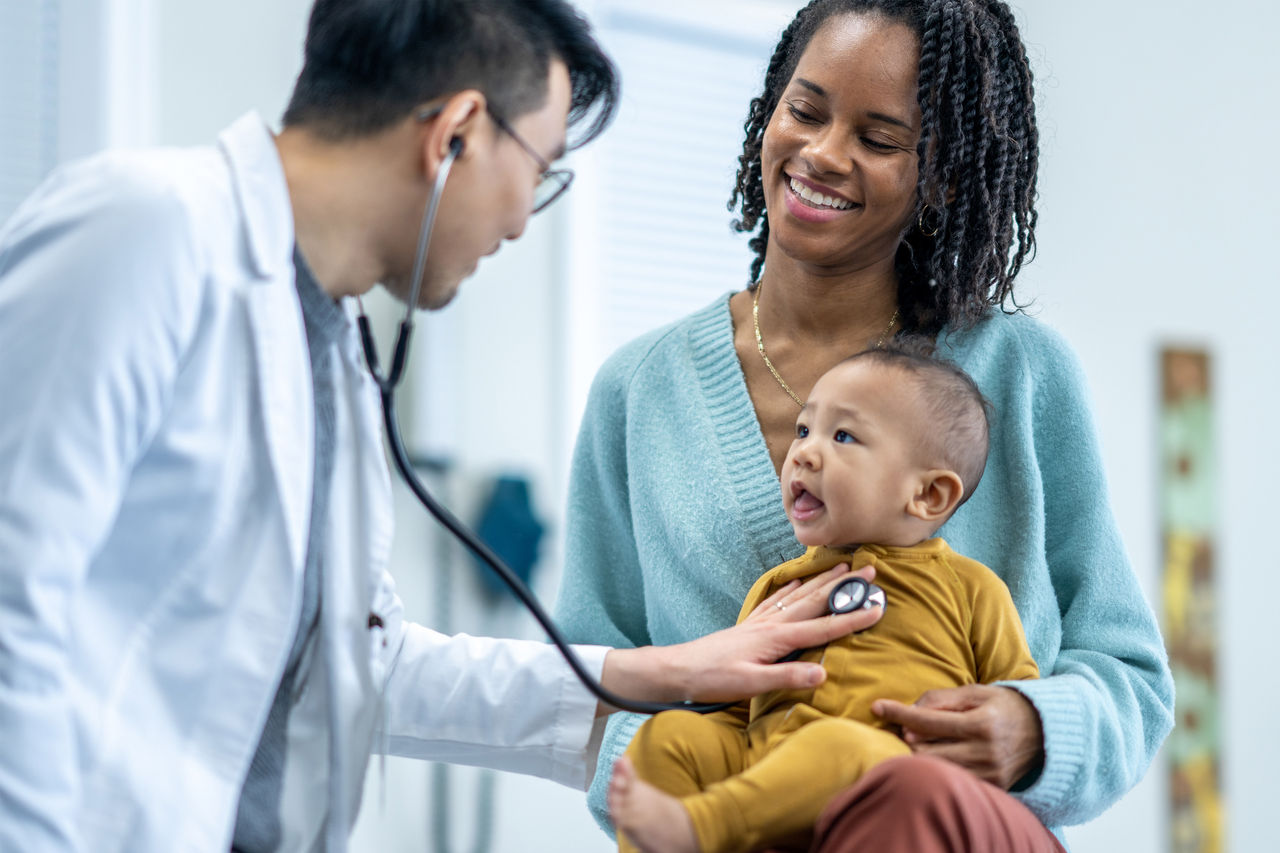 Doctor listening to the heart of a baby sitting on his mothers lap