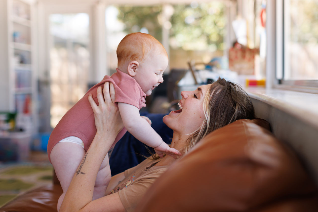 Mother holding baby in the air as they both smile at each other.