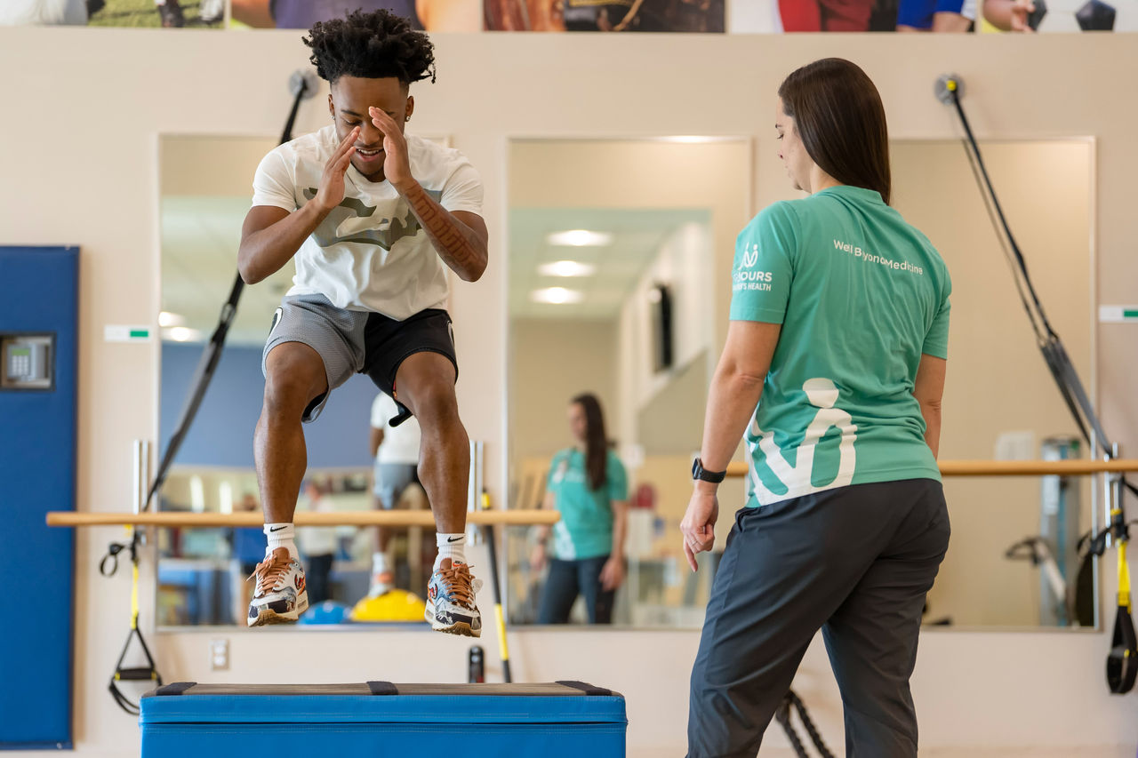 Teen boy athlete jumping in gym during physical therapy with a female provider