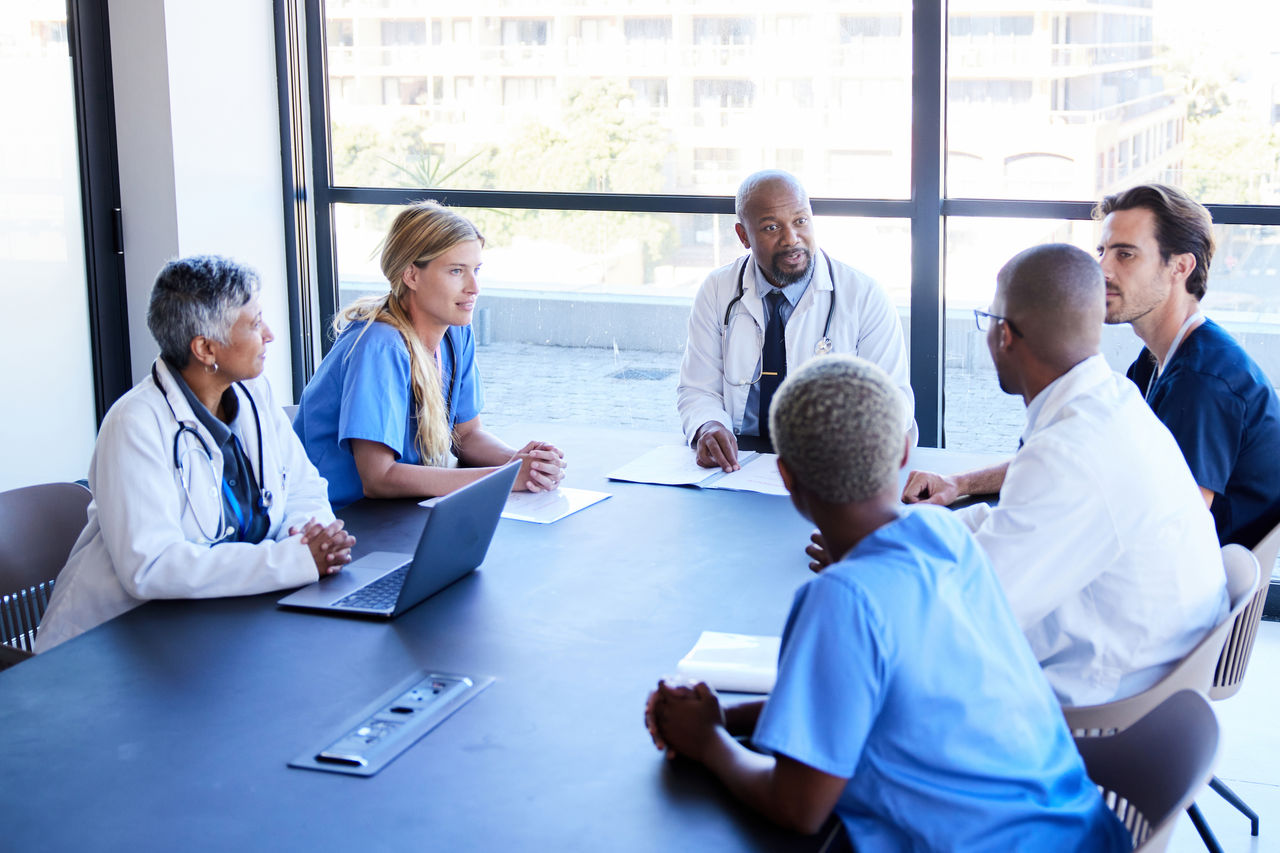 Group of medical staff meeting around a conference table in front of windows