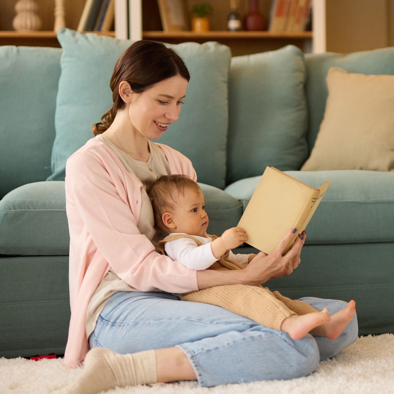 A mother kneeling on the floor reading to her infant.