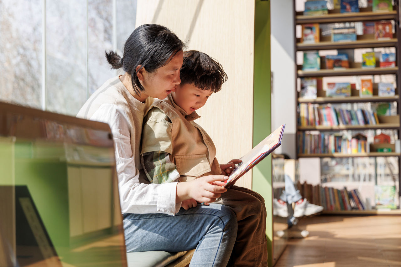 A mother reads to her 5 year old while he sits on her lap.