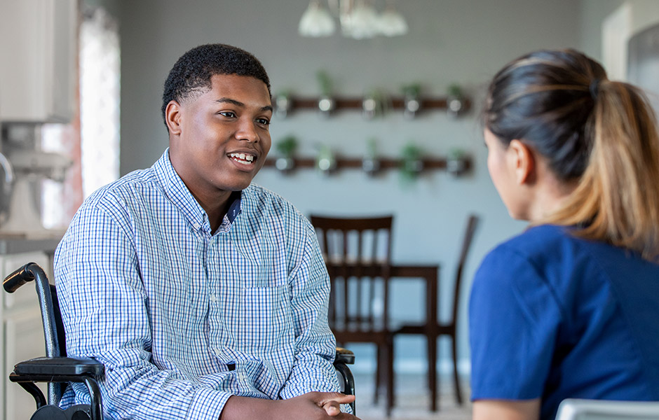 Teenage boy in wheelchair talks to female doctor in kitchen setting