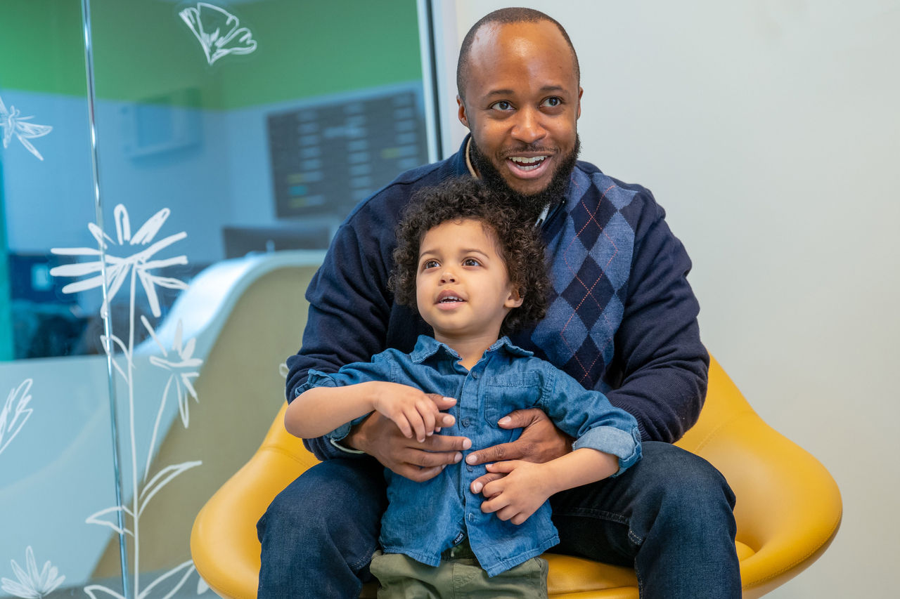 A father sitting in a chair hugging his standing son