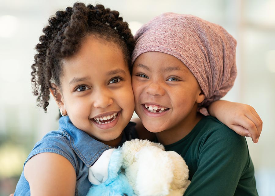 Two small children laugh and hug, one wears a head covering.