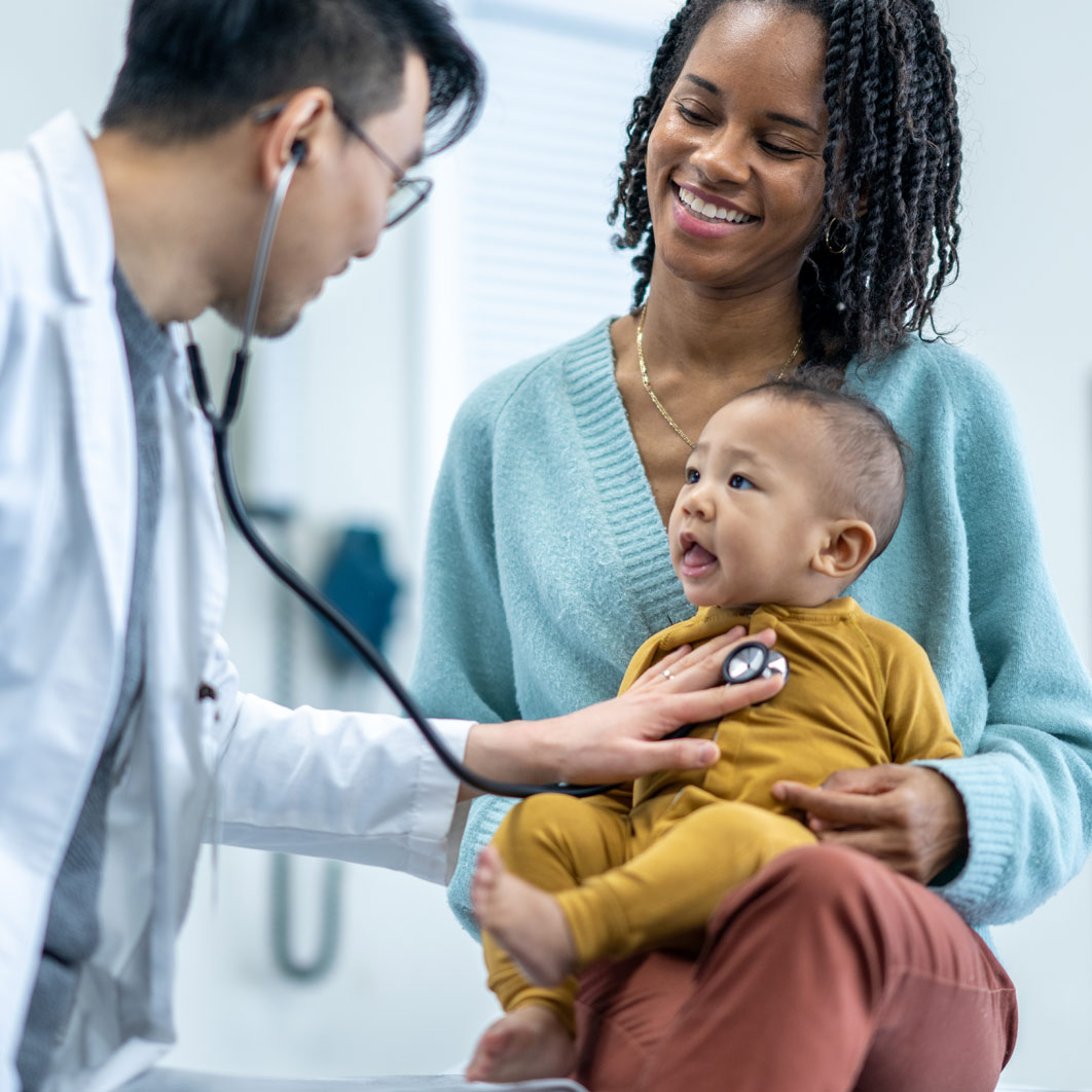 Doctor listening to the heart of a baby being held on his mothers lap