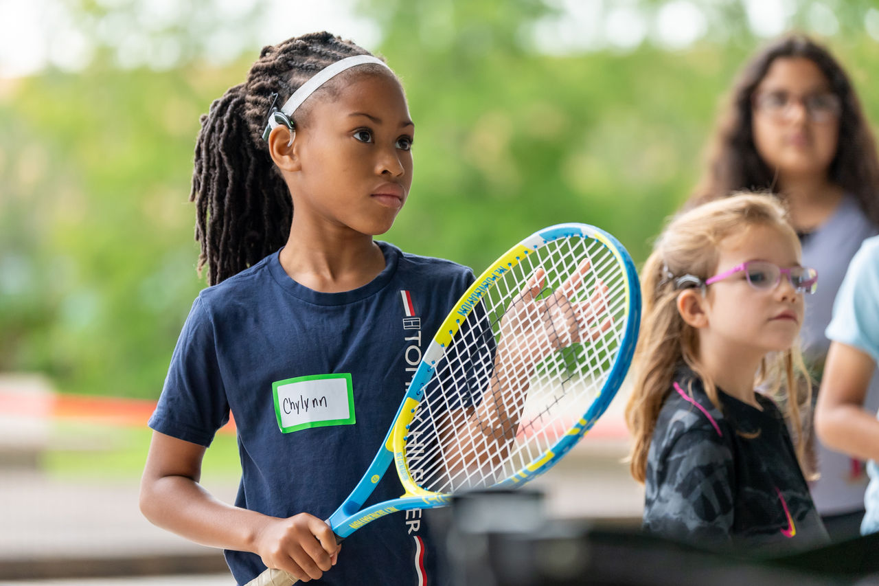 Young girl playing tennis at cochlear implant summer camp.