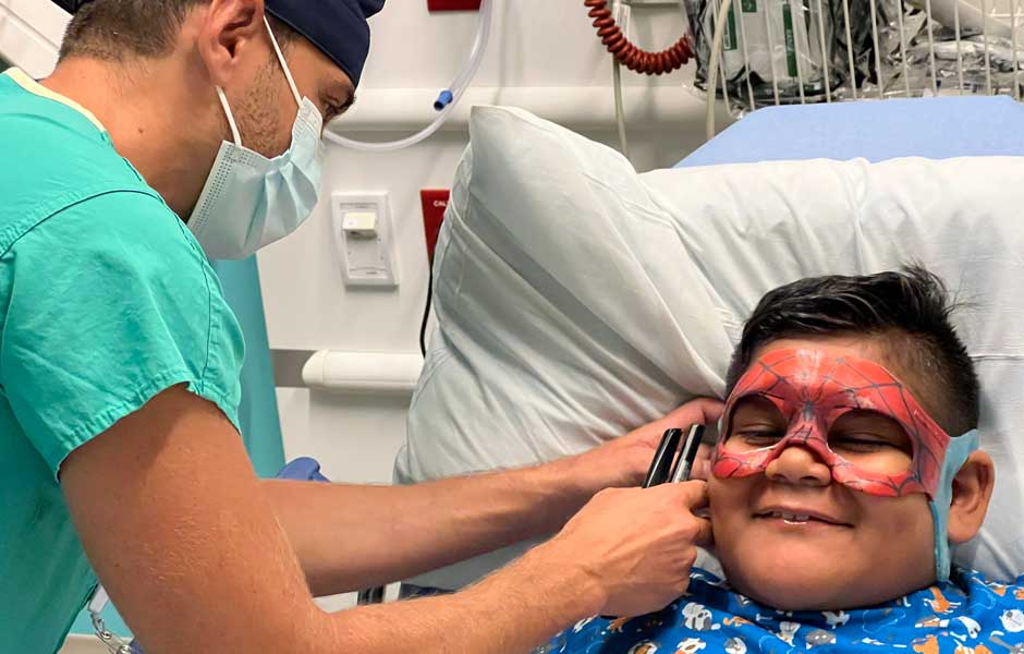 Boy wearing superhero mask while being examined by surgeon.