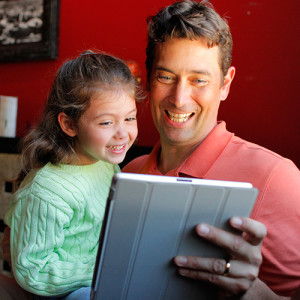Father and daughter reading on a tablet.